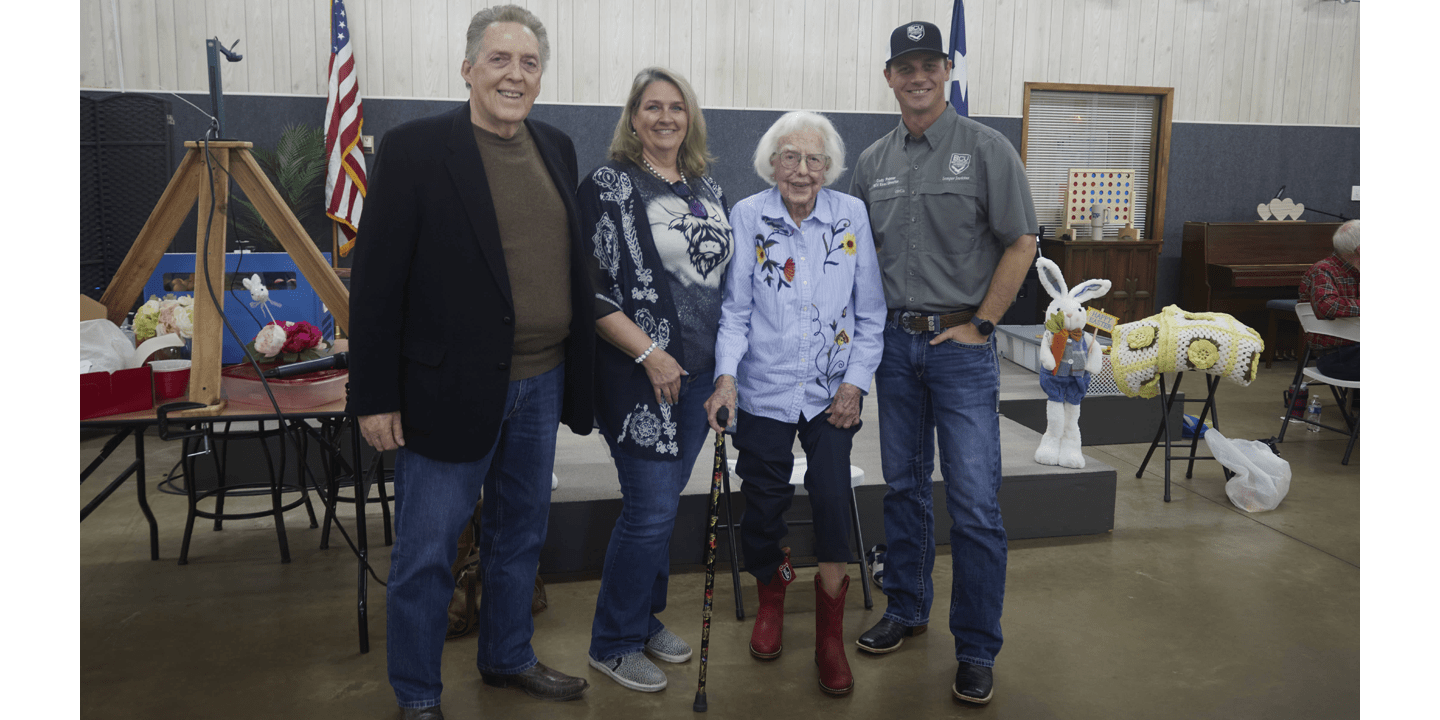 A few people from Justin Boots are posing with Jean Buford, who is presenting her boots. Jean is standing with a cane and showing off her new red boots by holding her pants legs up.
